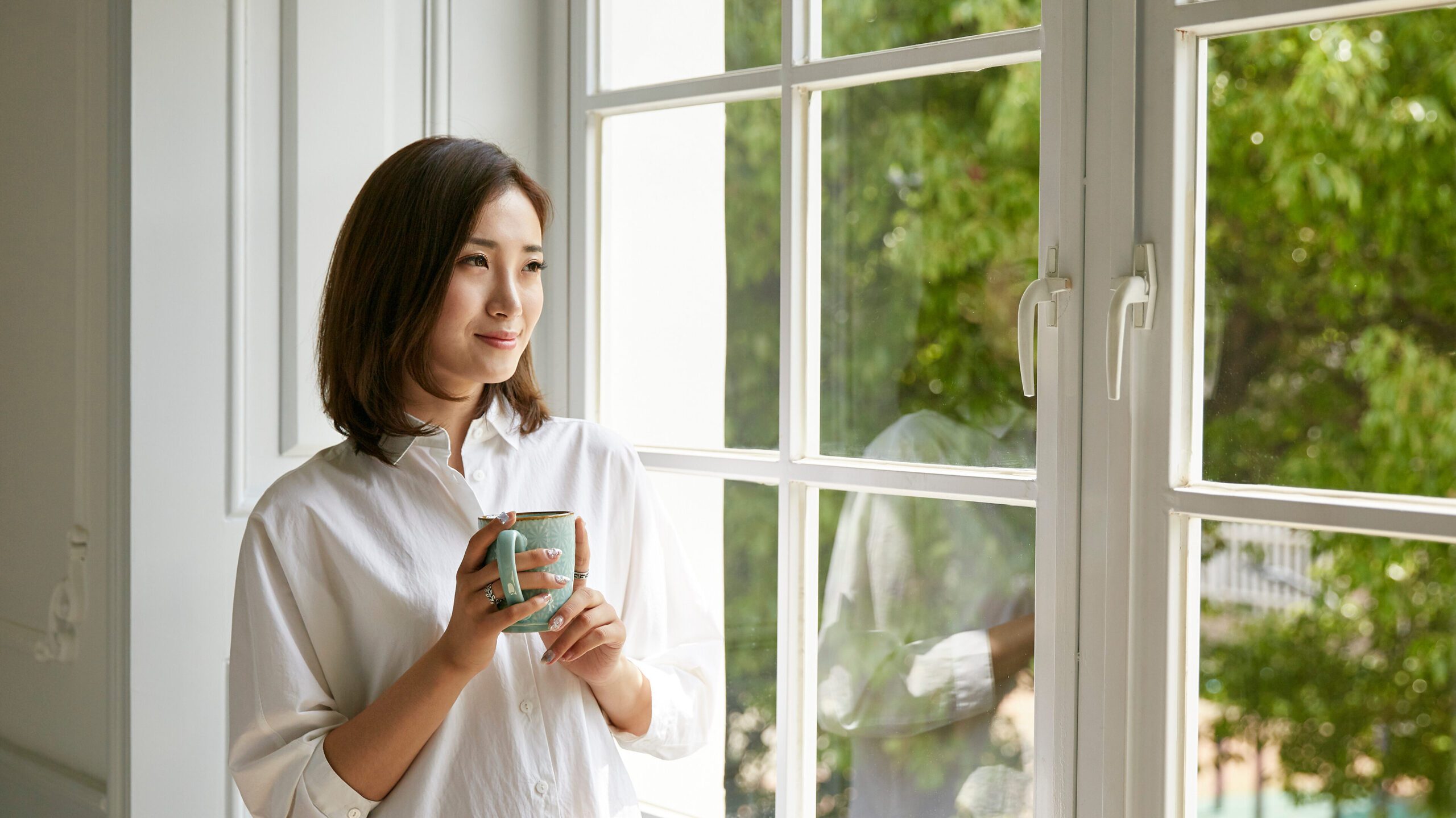 A woman is sipping tea staring out her window knowing that her peace of mind is a financial asset.